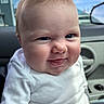 baby, child, face, smile, white_shirt, pink_pants, car_interior, window, car_door, cheeks, skin, expression, person, indoor, clothing, head, portrait, seat, hair, mischievous