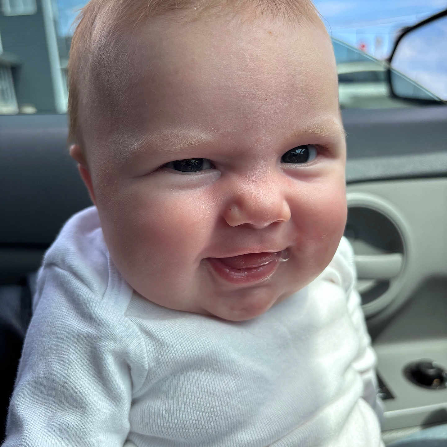 Lena is registered to the contest to win money with this photo: baby, child, face, smile, white_shirt, pink_pants, car_interior, window, car_door, cheeks, skin, expression, person, indoor, clothing, head, portrait, seat, hair, mischievous