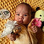 baby, baby_clothes, bee, child, cute, expressive_face, flower, hand, holding, indoors, infant, lying_down, milestone_card, newborn, pink_flower, plush_toy, portrait, soft_texture, white_flower, yellow_blanket
