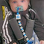 baby, pacifier, car_seat, adidas, tracksuit, child, blue_eyes, blanket, star_pattern, soft_toy, safety_harness, clothing, hand, face, indoor, cute, infant, person, seat, sparkles