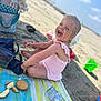 beach, blue_sky, bucket, child, daytime, food, happy, outdoor, plastic_container, playful, sand, smiling, snacks, summer, sunny, swimsuit, toddler, towel, toy, water_bottle