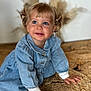 blonde_hair, blue_eyes, casual_clothing, child, cozy, crawling, cute, denim_dress, face, hands, indoors, natural_light, pampas_grass, pigtails, portrait, smiling, toddler, warm_colors, woven_mat, young_child
