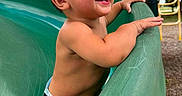 Ayce is registered to the contest to win money with this photo: toddler, child, playground, slide, smiling, happy, outdoor, summer, fun, park, bare_chested, green_slide, play_equipment, daylight, joyful, person, leisure, nature, casual, active