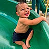 toddler, child, smiling, playground, slide, green_slide, outdoor, park, happy, bare_chest, shorts, feet, play, fun, young_child, daylight, nature, grass, trees, summer