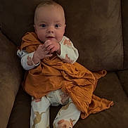 Merliah joined the competition — help win amazing prizes! baby, infant, child, couch, blanket, pajamas, animal_print, footwear, face, hands, sitting, indoors, cute, cozy, expression, clothing, furniture, brown, orange, portrait