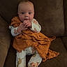 baby, infant, child, couch, blanket, pajamas, animal_print, footwear, face, hands, sitting, indoors, cute, cozy, expression, clothing, furniture, brown, orange, portrait