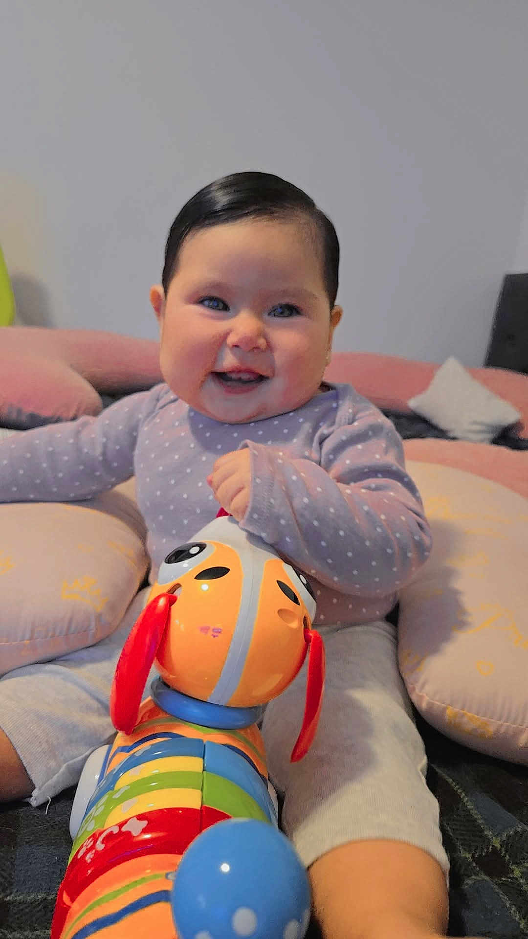 Arleth is registered to the contest to win money with this photo: baby, child, smiling, toy, colorful_toy, indoor, cushion, happy, face, person, sitting, clothing, pants, long_sleeve, cute, playful, infant, home, fun, bright