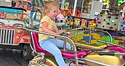 Eliana is registered to the contest to win money with this photo: amusement_ride, background, blue_jeans, carnival, child, colorful, excitement, fair, fun, lights, metal_railings, motion_blur, motorcycle_ride, outdoor, playful, purple_canopy, smiling, white_shoes, yellow_shirt, young_child