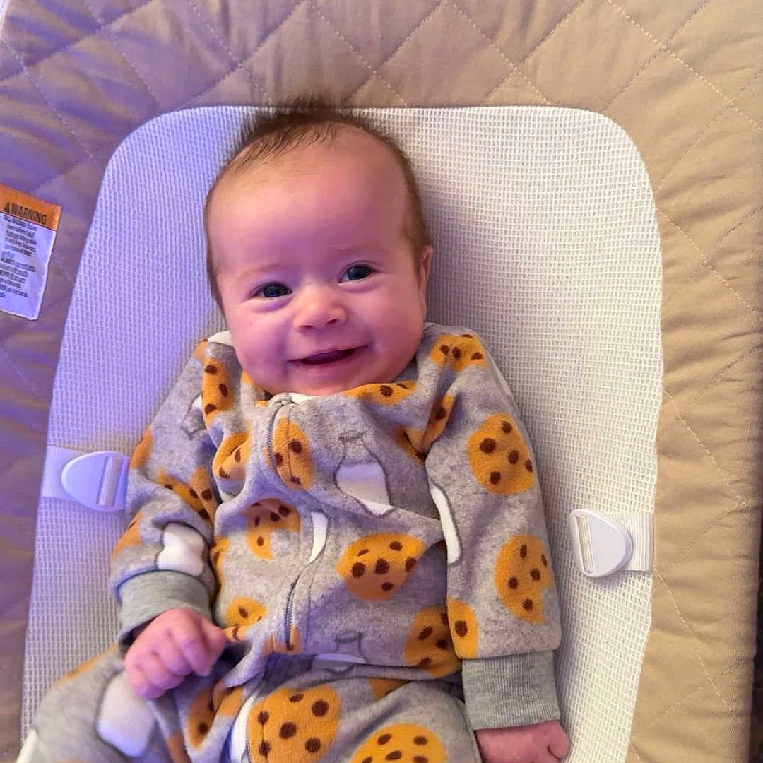 Andrew is registered to the contest to win money with this photo: baby, smiling, onesie, cookie_pattern, infant, child, seat, cushion, fabric, happy, indoors, cute, small, young, relaxing, person, baby_gear, comfort, portrait, cozy