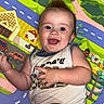 baby, child, smiling, play_mat, colorful, indoor, happy, infant, cute, person, clothing, skin, face, head, hand, legs, toy, background, pattern, diaper