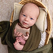 Aron a rejoint le concours — aidez-le/la à gagner de superbes lots ! baby, newborn, infant, basket, blanket, knitwear, bead_necklace, blue_eyes, swaddle, pillow, wooden_floor, toes, hands, portrait, studio, cozy, soft_texture, cute, wicker, peaceful