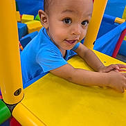 Kordell is registered to the contest to win money with this photo: child, toddler, baby, face, smiling, happy, playground, indoor, play_structure, yellow, blue, colorful, ball_pit, plastic, portrait, arms, hands, eyes, playtime, joy