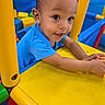 child, toddler, baby, face, smiling, happy, playground, indoor, play_structure, yellow, blue, colorful, ball_pit, plastic, portrait, arms, hands, eyes, playtime, joy