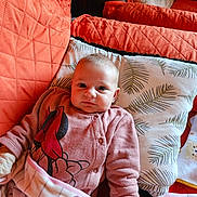 Stella participe au concours pour gagner de l'argent avec cette photo : baby, infant, pillow, blanket, cushion, orange, pink, clothing, face, person, indoor, cute, young_child, lying_down, patterned, cartoon_character, soft_texture, comfortable, resting, cozy