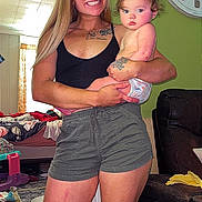 Whitley joined the competition — help win amazing prizes! baby, infant, woman, adult, smiling, portrait, holding_baby, indoor, living_room, wall_clock, couch, furniture, tattoo, clothing, diaper, toy, rug, household, family, photograph