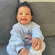 Ena a rejoint le concours — aidez-le/la à gagner de superbes lots ! baby, child, smiling, happy, sitting, couch, clothing, sock, footwear, hand, face, indoor, cute, infant, curly_hair, playful, cozy, daisy_pattern, home, portrait