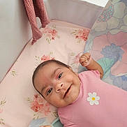 Sofia participe au concours pour gagner de l'argent avec cette photo : baby, bed, blanket, child, crib, cute, face, floral_pattern, hands, happy, head, indoor, infant, knitted_cloth, lying_down, newborn, pink_onesie, portrait, smiling, soft_toys
