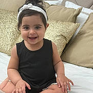 Célia participe au concours pour gagner de l'argent avec cette photo : baby, child, smile, headband, black_top, bed, pillow, gold_pillow, beige_pillow, happy, sitting, indoors, person, cute, hair, face, skin, furniture, blanket, cozy
