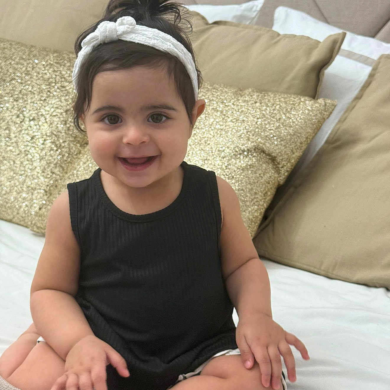 Célia participe au concours pour gagner de l'argent avec cette photo : baby, bed, beige_pillow, black_top, blanket, child, cozy, cute, face, furniture, gold_pillow, hair, happy, headband, indoors, person, pillow, sitting, skin, smile