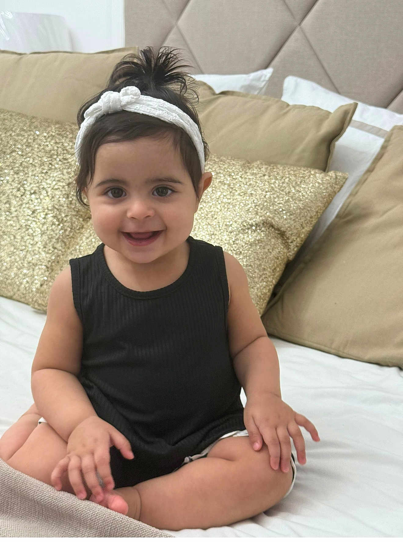Célia participe au concours pour gagner de l'argent avec cette photo : baby, child, smile, headband, black_top, bed, pillow, gold_pillow, beige_pillow, happy, sitting, indoors, person, cute, hair, face, skin, furniture, blanket, cozy