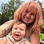 Phoenix is registered to the contest to win money with this photo: woman, baby, smiling, tattoos, outdoor, trees, green_bottle, happy, person, nature, daylight, face, hair, skin, holding, laughing, casual_clothing, bench, family, portrait