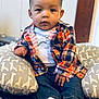 baby, child, indoor, plaid_shirt, dinosaur_tee, giraffe_pillow, cushion, denim_jeans, socks, cute, portrait, seated, expression, hands, face, eyes, wooden_door, fabric, cozy, casual_clothing