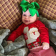 Lainey joined the competition — help win amazing prizes! baby, child, smiling, green_bow, red_shirt, striped_pants, plaid_couch, blanket, cozy, indoor, holiday, christmas, cute, infant, happy, portrait, relaxing, soft_texture, clothing, headband