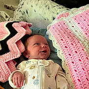 Lainey joined the competition — help win amazing prizes! baby, infant, blanket, crochet, pink, black, white, dog, spotted_dog, pet, sleeping_area, comfort, clothing, smile, face, hand, lying_down, cozy, soft, indoor