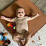 animal_print, arms_spread, baby, child, colorful, cute, face, floor_mat, flooring, happy, indoor, infant, legs_spread, lying_down, onesie, patterned_mat, person, playtime, smiling, toy