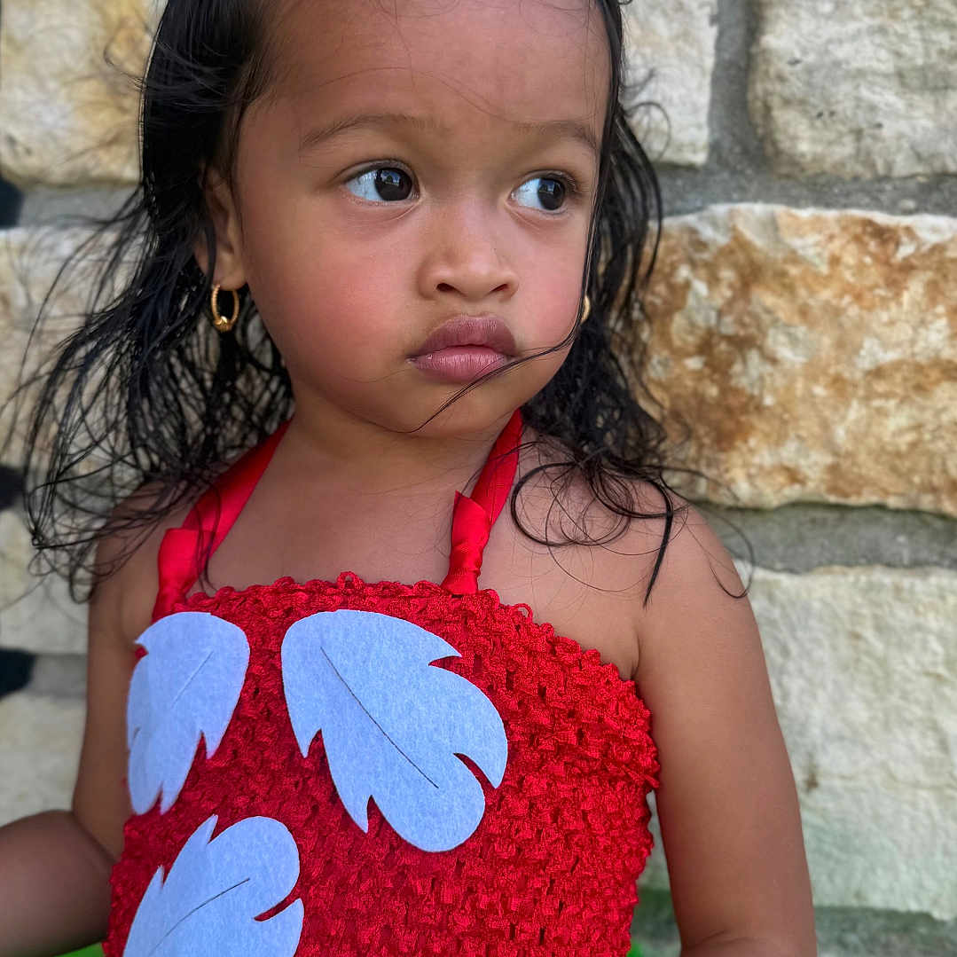 Avianna Singh Luna joined the competition — help win amazing prizes! child, closeup, colorful_clothing, curly_hair, cute, earrings, fashion, girl, green_tutu, hair_tie, nature_background, outdoor, person, portrait, red_dress, serious_expression, stone_wall, summer, toddler, young_child