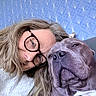blue_wallpaper, casual, close_up, comfort, companion, cozy, dog, expression, face, friendly, geometric_pattern, glasses, head, human, indoor, pet, portrait, relaxed, snuggling, woman