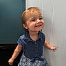 blue_dress, buttoned_shirt, carpet, child, cute, denim, door, dress, face, floral_pattern, happy, indoor, person, portrait, short_hair, smiling, standing, toddler, wall, young_child