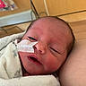 Nova is registered to the contest to win money with this photo: newborn, baby, infant, blanket, swaddle, face, medical_tape, hospital, resting, sleepy, closeup, skin, head, person, indoors, human, comfort, care, young_child, portrait