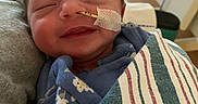 Nova is registered to the contest to win money with this photo: newborn, baby, infant, smiling, hospital, feeding_tube, blanket, striped, wrapped, sleeping, person, closeup, face, cheek, clothing, hand, indoor, care, health, resting