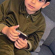 Richard a rejoint le concours — aidez-le/la à gagner de superbes lots ! child, boy, olive_green_clothing, smartphone, sitting, couch, gray_couch, indoors, curious, young, portrait, casual, holding, technology, home, furniture, person, face, hair, expression