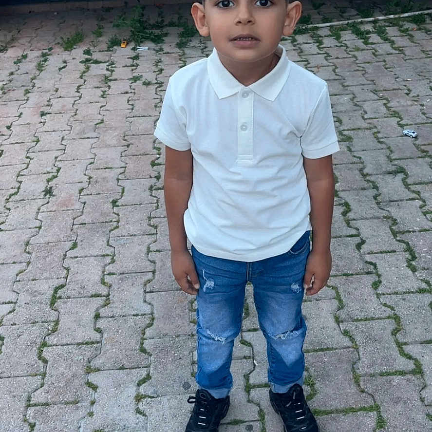Richard participe au concours pour gagner de l'argent avec cette photo : child, boy, standing, white_polo_shirt, blue_jeans, black_shoes, outdoor, pavement, vehicle, curious_expression, portrait, casual_clothing, young, person, street, daylight, sidewalk, urban, background, human