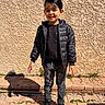 Richard participe au concours pour gagner de l'argent avec cette photo : child, boy, standing, black_jacket, jeans, shoes, outdoor, sunlight, shadow, brick_pavement, wall, smiling, happy, casual_clothing, hair, person, daylight, urban, texture, young