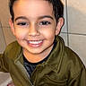 child, boy, smile, face, hair, jacket, zipper, clothing, portrait, indoor, tile, wall, happy, person, skin, eyebrows, teeth, eyes, hand, casual
