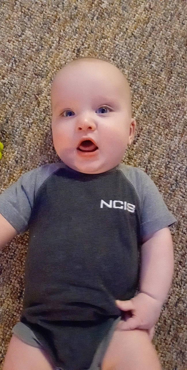 River is registered to the contest to win money with this photo: baby, baby_laughing, baby_toddler_clothing, cheek, child, eye, fun, grass, happy, laugh, long_sleeved_t_shirt, nose, person, portrait_photography, sitting, sleeve, smile, surprise, t_shirt, toddler