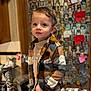 child, boy, plaid_shirt, tan_pants, indoor, kitchen, bottle_openers, collection, wall, curly_hair, standing, portrait, furniture, cabinet, countertop, decor, person, casual_clothing, curious, young