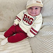 Andrea a rejoint le concours — aidez-le/la à gagner de superbes lots ! baby, infant, smiling, hat, cap, sweatshirt, text_on_clothing, pants, socks, sofa, cushion, beige, striped_texture, cozy, portrait, cute, cheeks, handmade_label, drool, sitting