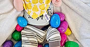 Carter joined the competition — help win amazing prizes! baby, bib, blanket, child, colorful, cozy, cute, easter_eggs, face, holiday_theme, indoors, infant, person, plastic_eggs, playful, smiling, soft_texture, striped_pants, yellow_hat, yellow_slippers