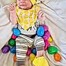 Carter joined the competition — help win amazing prizes! baby, child, infant, yellow_hat, yellow_slippers, striped_pants, plastic_eggs, easter_eggs, blanket, soft_texture, cute, smiling, indoors, playful, colorful, holiday_theme, cozy, bib, face, person