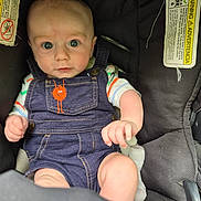 Carter is registered to the contest to win money with this photo: baby, baby_face, car_seat, child, clothing, curious, cute, denim_overalls, hands, indoors, infant, person, portrait, seated, sitting, soft_toy, striped_shirt, warning_label, wide_eyes, young_child