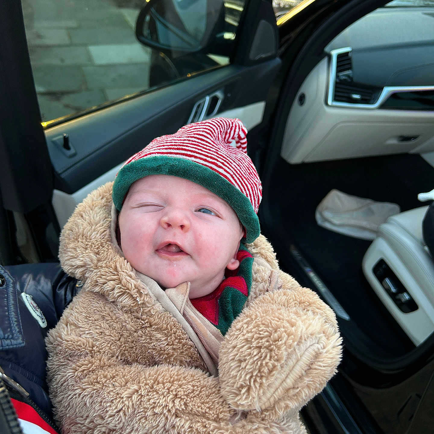 Imran is registered to the contest to win money with this photo: baby, car, car_door, child, coat, cute, face, fluffy_coat, hat, holding, infant, outdoor, person, portrait, smiling, striped_hat, vehicle_interior, warm_clothing, winking, winter_clothing