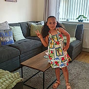 Milania joined the competition — help win amazing prizes! carpet, child, coffee_table, curtains, cushions, floral_dress, framed_photo, girl, home_decor, indoors, living_room, peace_gesture, peace_sign, person, sandals, smiling, sofa, standing, window, wooden_floor