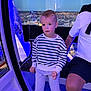 child, boy, striped_sweater, pants, indoor, blue_lighting, cityscape, window, night, adult, shorts, seat, ferris_wheel, observation_pod, expression, curious, person, casual_clothing, hand, leg