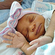 Ariyah is registered to the contest to win money with this photo: apparel, baby, blanket, bottle, bow_hat, closeup, cozy, cute, face, hand, indoors, infant, newborn, peaceful, person, portrait, resting, skin, sleeping, soft_lighting