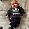 baby, infant, smile, adidas, clothing, black_outfit, socks, blanket, fabric, cute, lying_down, portrait, child, soft_texture, casual_wear, indoors, happy, young_child, comfortable, small_hands