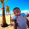 baby, child, person, beach, sand, palm_tree, sky, outdoor, sunny, clothing, overalls, blue_sky, summer, vacation, nature, portrait, holding, hand, toddler, casual